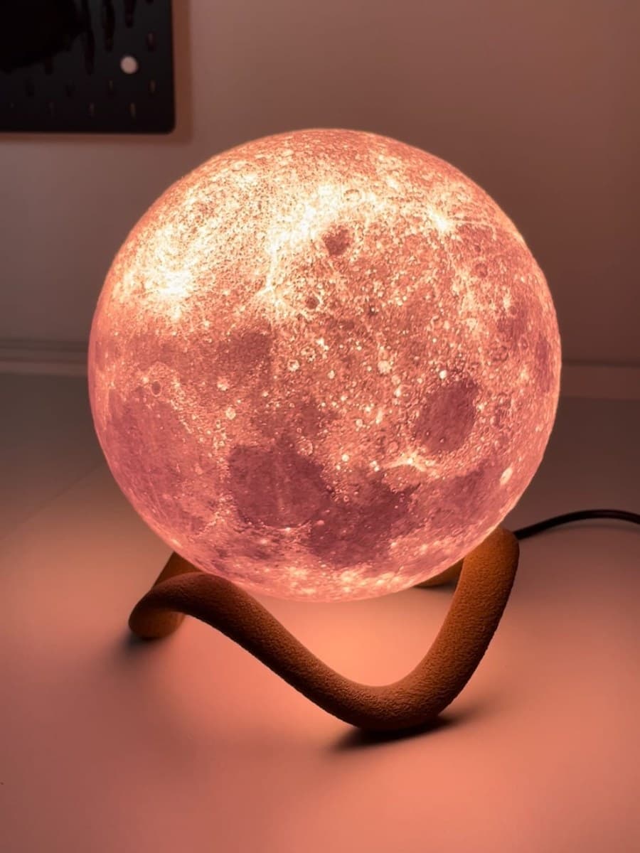 Moon lamp on curved wooden stand with warm pink-amber glow
